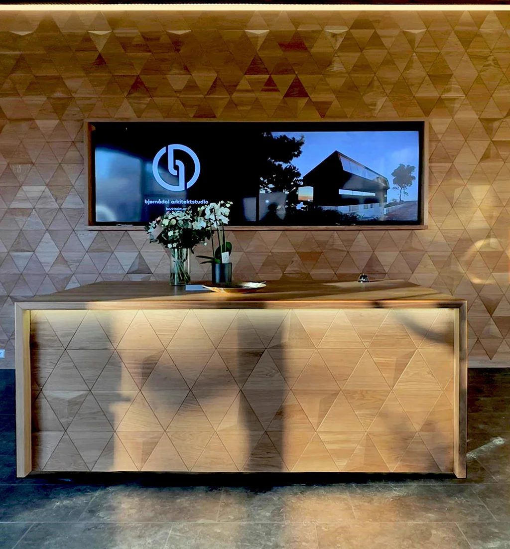 Modern reception desk and wall in an architectural studio covered with oak triangular wood panels.