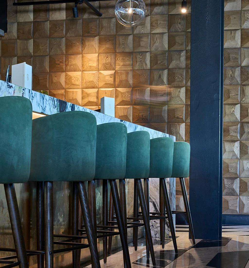 Luxury bar interior featuring a marble counter, blue velvet stools, and a feature wall made of square 3D oak wood panels.